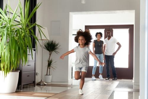 Excited little funny african girl running exploring big modern house moving in_ happy black parents and kid daughter coming into new home_ cute mixed race child having fun in hallway_ family mortgage