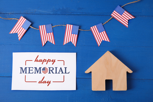 Greeting card for Memorial Day celebration with figure of house and USA flags on color wooden background