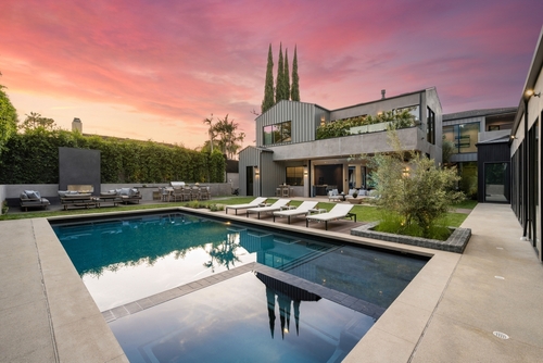 Modern luxury home with a swimming pool and outdoor seating area at sunset.