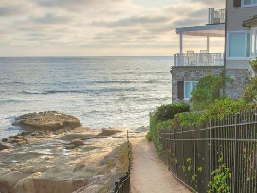 Square White puffy clouds Dirt path near the water at La Jolla in California. Pathway with railings and a view of the pacific ocean at the left and beach house on the right against the sunset sky.
