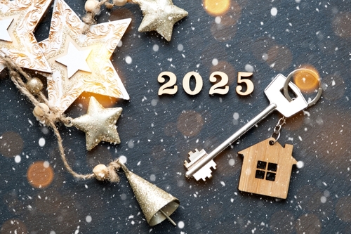 House key with keychain cottage on festive black background with stars_ lights of garlands. New Year 2025 wooden letters_ greeting card. Purchase_ construction_ relocation_ mortgage_ insurance