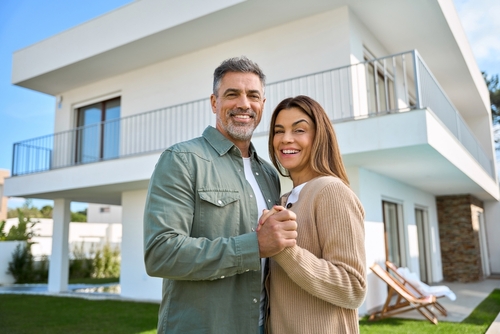 Portrait of happy smiling mature older family couple new property buyers modern dream luxury villa owners standing outside house_ affectionate senior middle aged man and woman in love hugging outdoor.