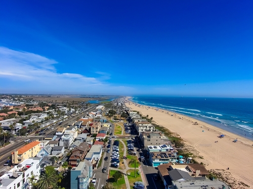 aerial shot of a gorgeous summer landscape along the coastline with blue ocean water_ brown sand_ and homes along the beach with blue sky at Long Beach City Beach in Long Beach California USA