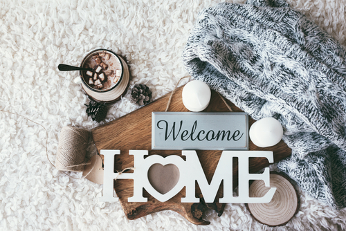 Winter homely scene_ scandinavian style. Warm knit sweater_ candles_ cup of sweet cocoa with marshmallows and other decor on tray in bed. Wooden craft letters Welcome Home. Lazy cold weekend.