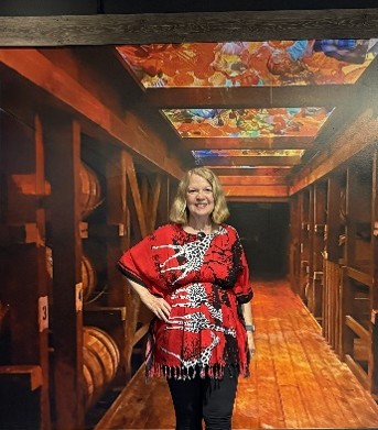 OLLI member, Brenda Mannino, stands inside of a barrel room with stained glass ceiling at the Maker's Mark distillery.