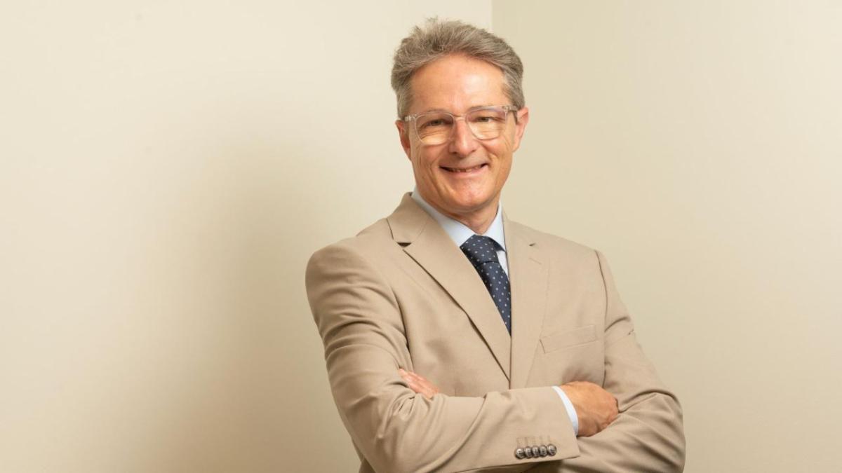 Man in a tan suit stands in front of a neutral background