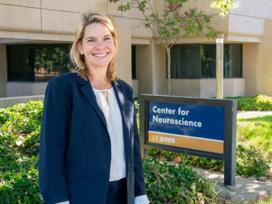 Smiling woman in blazer stands outside UC Davis Center for Neuroscience building beside center’s sign