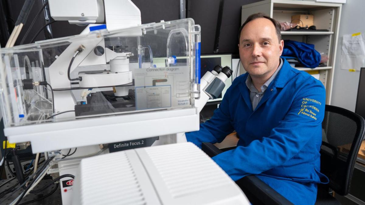 Researcher in a UC lab coat sits beside advanced microscope equipment preparing for imaging work in the laboratory