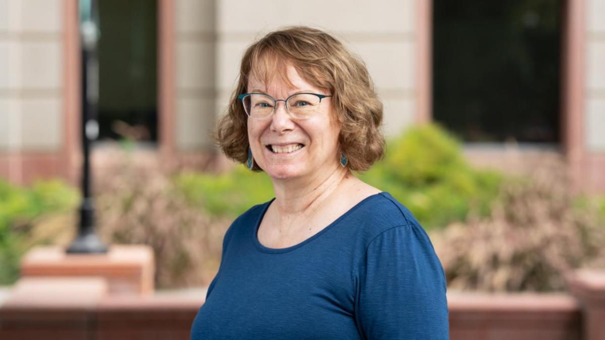 A smiling woman in a blue shirt standing outside