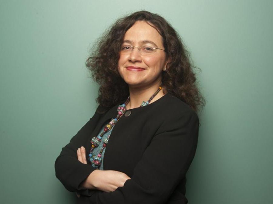 Portrait of a woman in glasses standing in front of a teal background