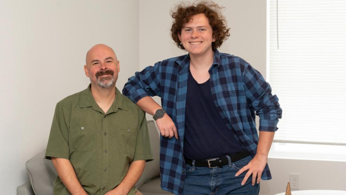 Two smiling people in a living room one seated and one standing