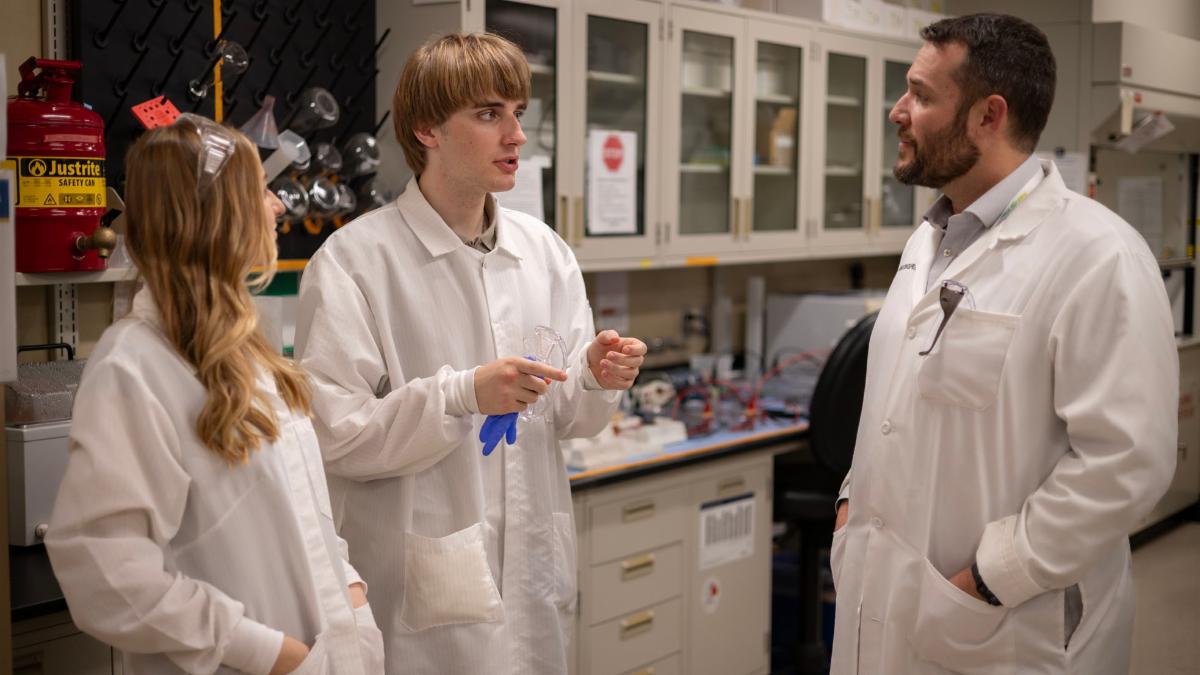 Three people in lab coats standing in a research lab talking