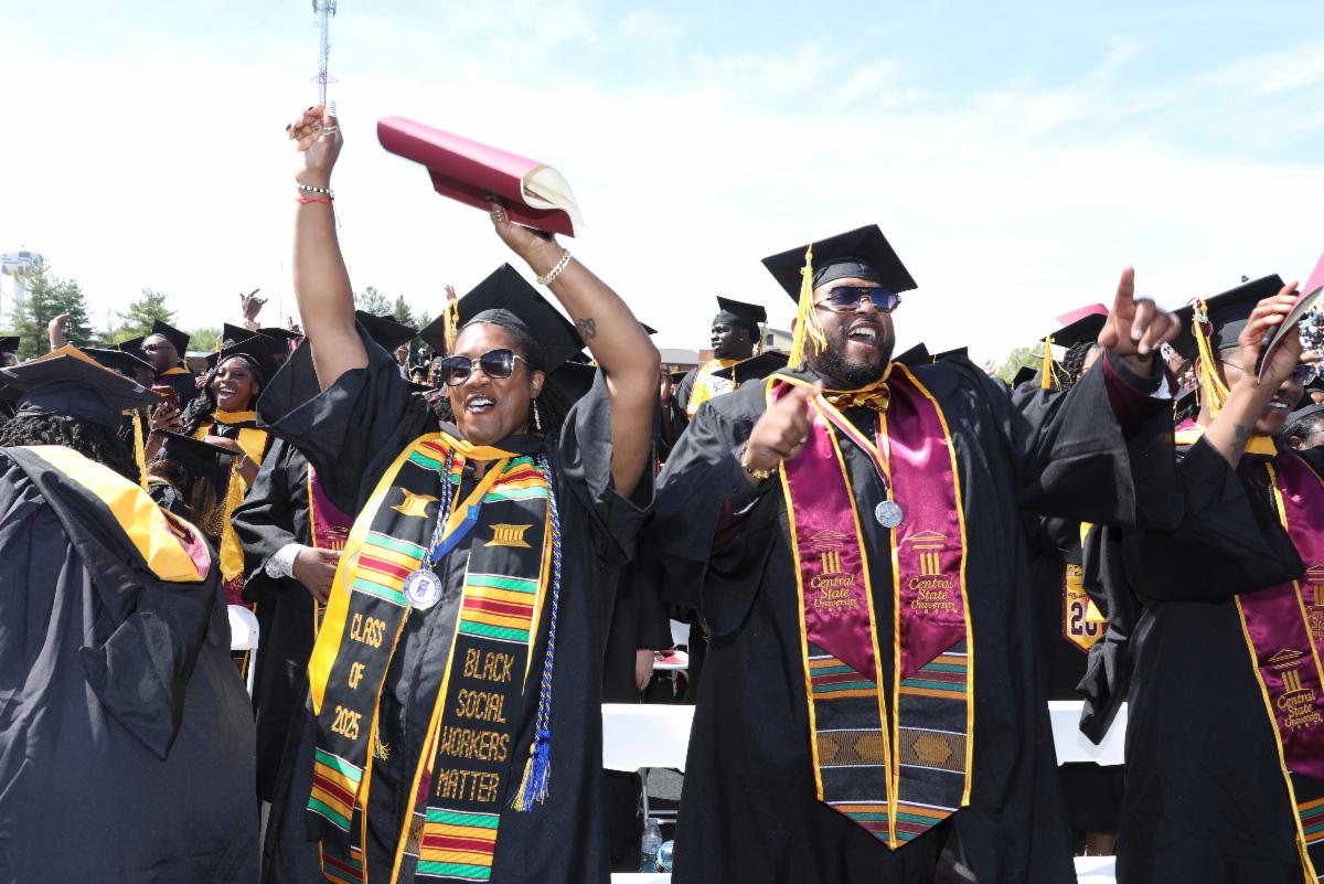 graduates in cap and gown celebrate with hands in the air