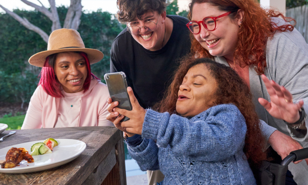 A group of people with and without disabilities taking a selfie while having dinner on a patio.