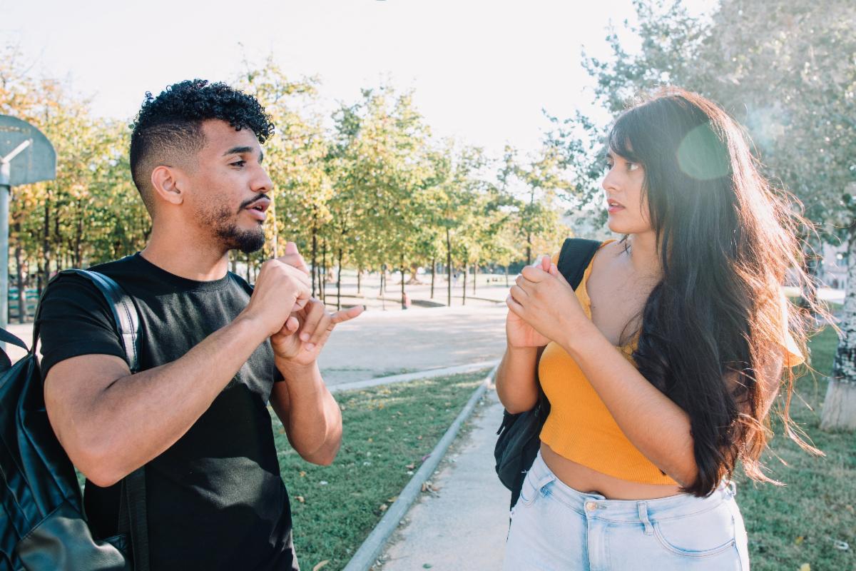A young man and woman with back packs using sign language.