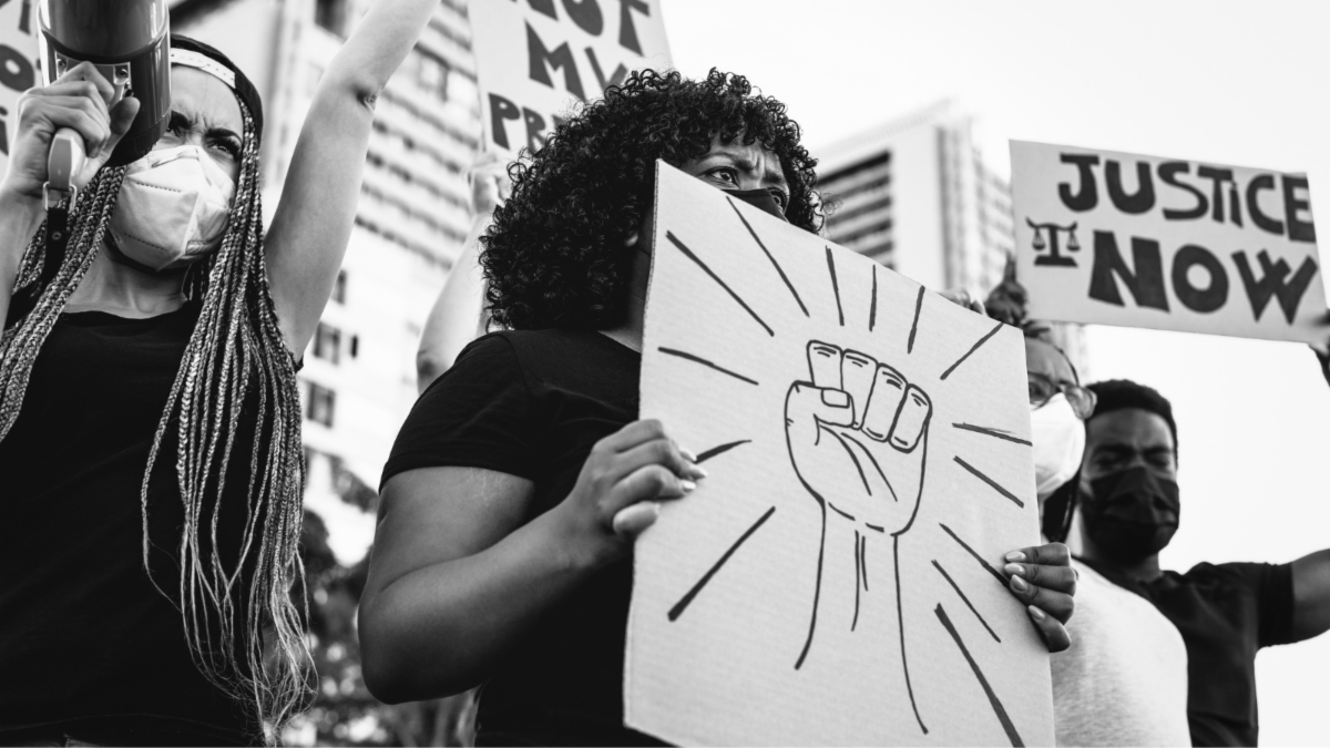 Black Americans in the street holding signs depicting resistance and saying justice now.