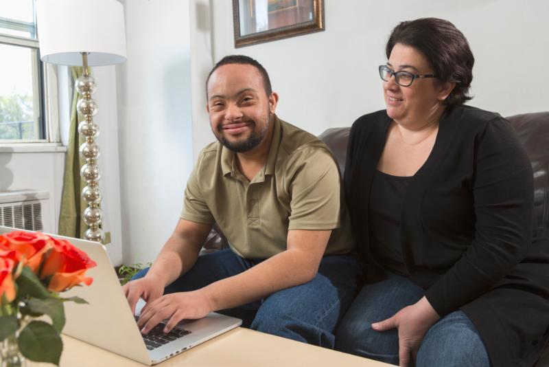 African American man with Down Syndrome using a laptop with his mother at home