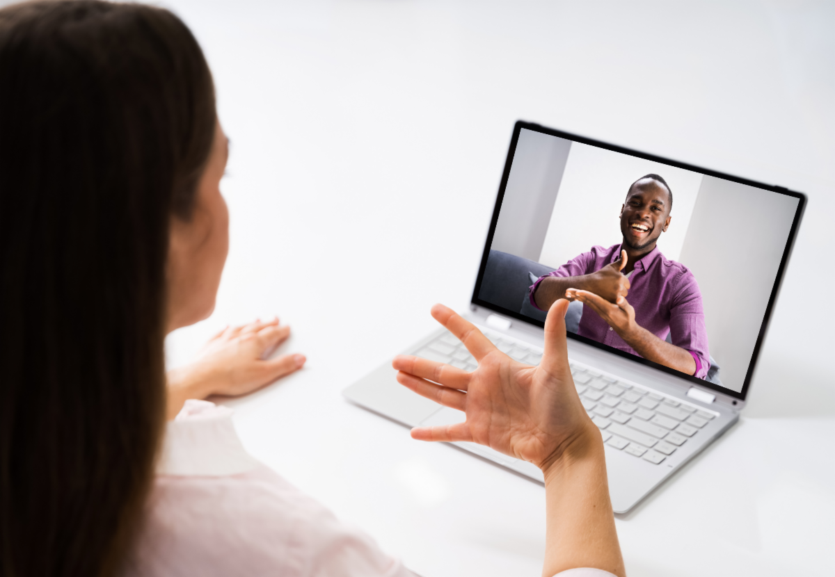 A person communicating via sign language with someone on a laptop.