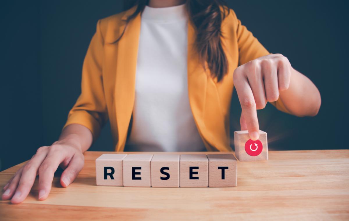 A woman at a table with wooden blocks that spell reset and a block with a refresh icon.
