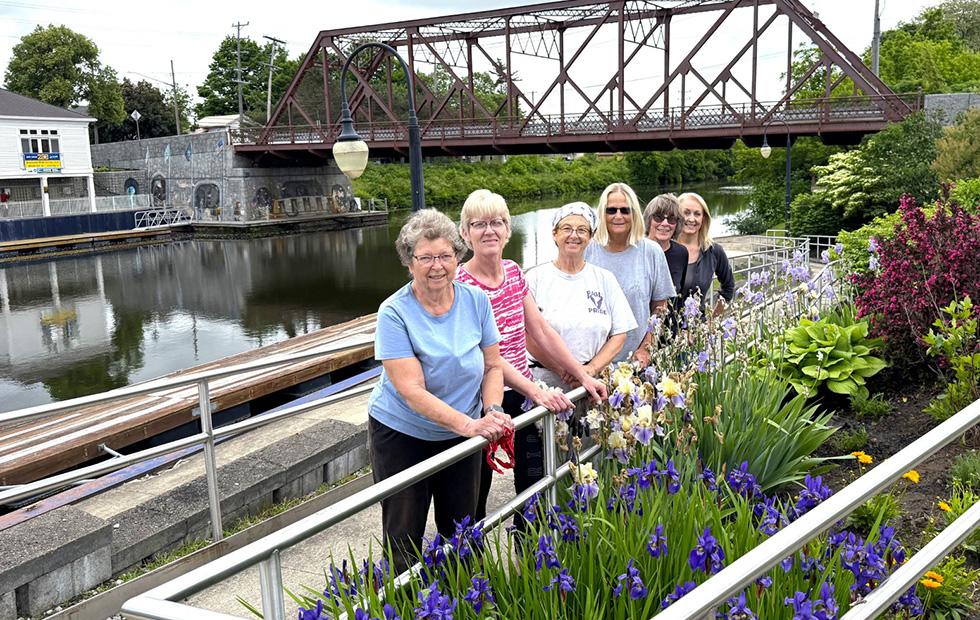 A group of gardening volunteers stand by a colorful garden along the Erie Canal in Newark.