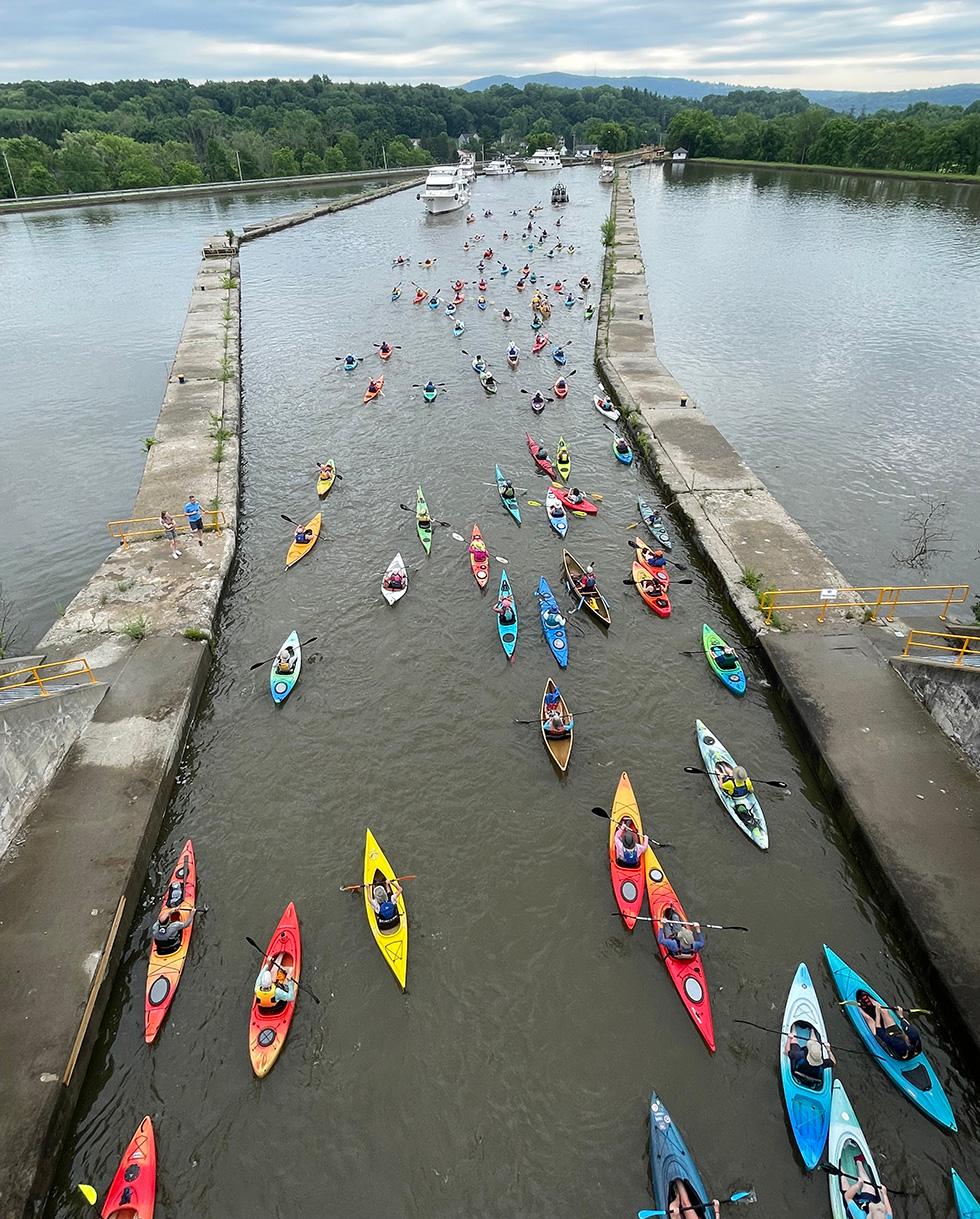 A large group of kayaks funnels through a channel between locks E5 and E4 of the Erie Canal during an event.