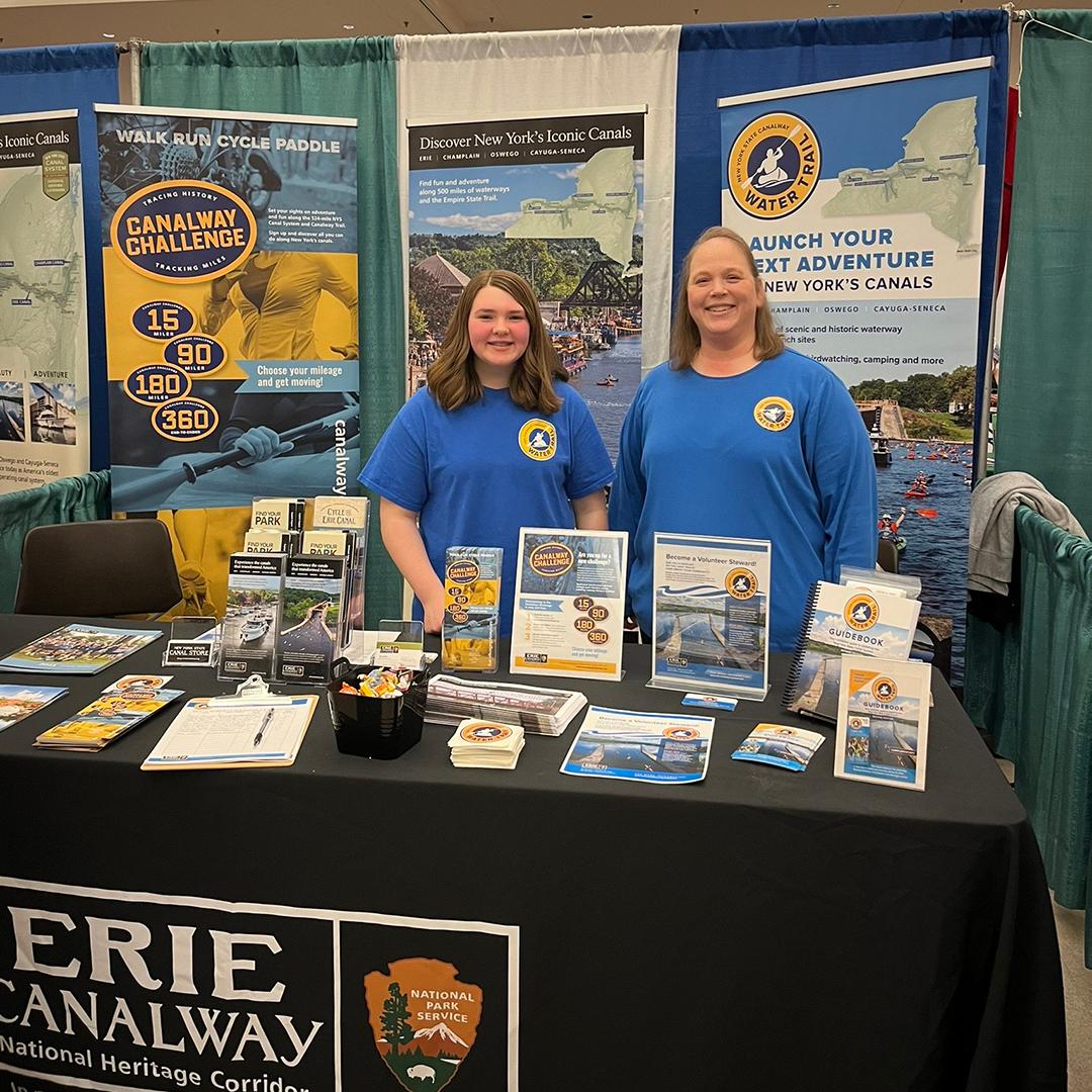 Two woman standing behind the Erie Canalway booth at the Upstate Summer Expo.