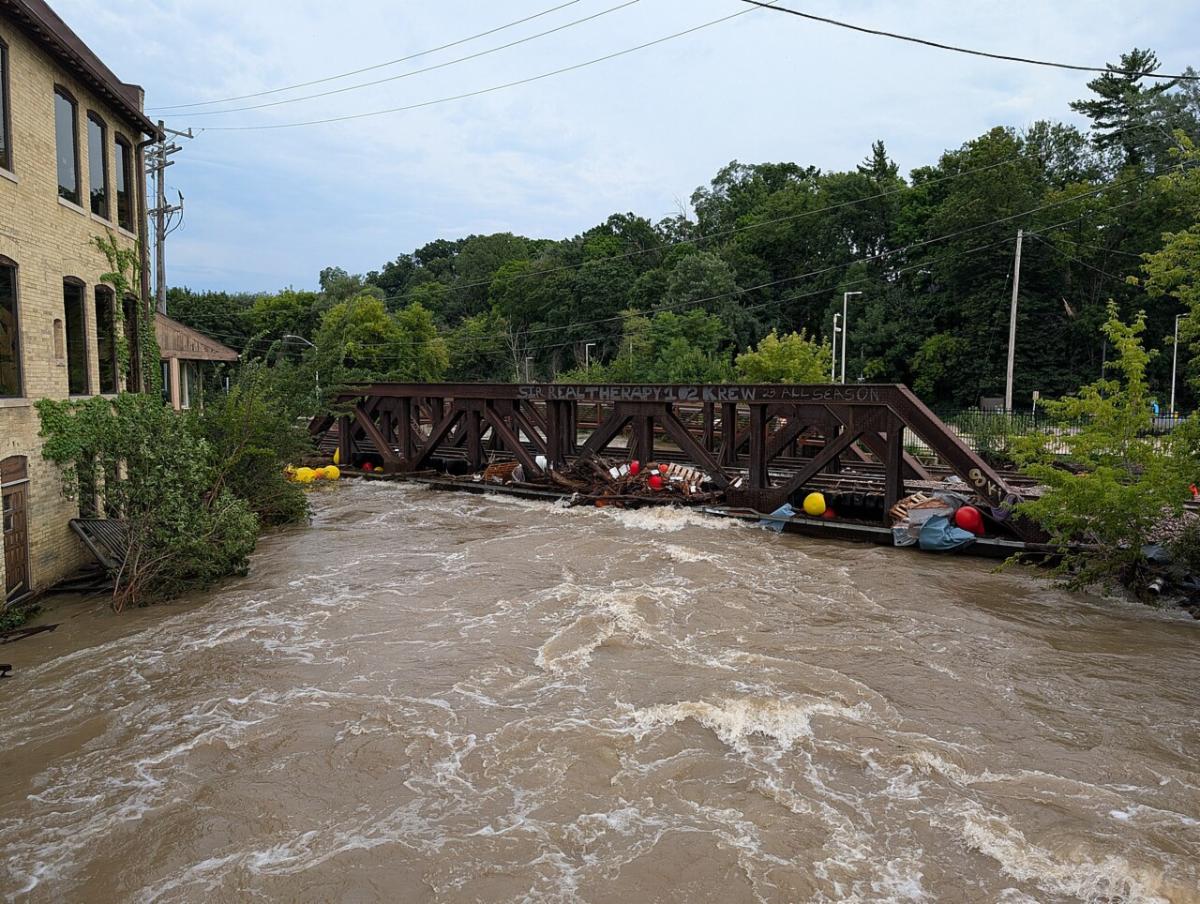 A river overflows it's banks and pushes debris up against a railroad bridge.