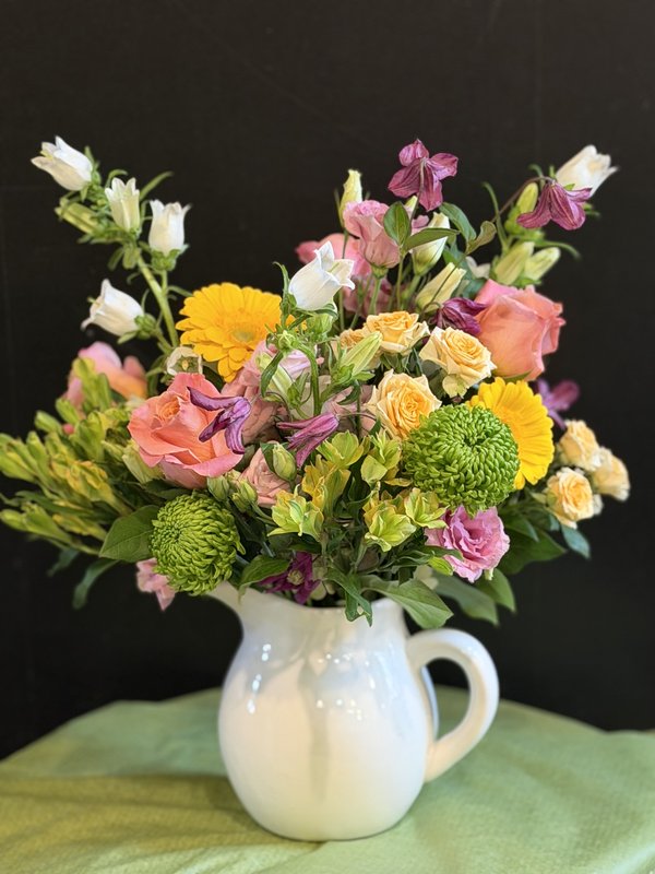 Wildflower Whimsy — cheerful mix of soft pinks, yellows, greens and purples in a white ceramic pitcher