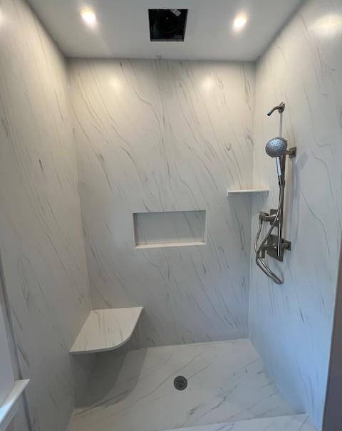 Interior of a while marble shower with built in shelves and a seat
