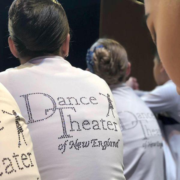 Image of a girl the back of her white shirt says dance theater of new england in rhinestones