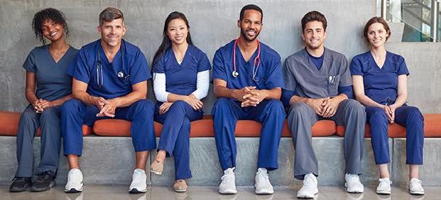 Nurses in scrubs sitting in a row on a bench