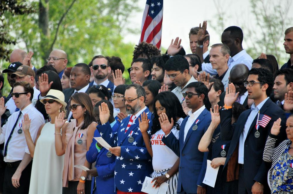 A diverse group of adults stand with right hand in air as they take the oath.