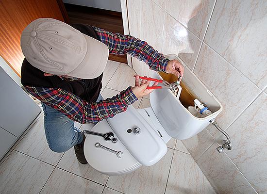 Man in hat fixing leaky toilet