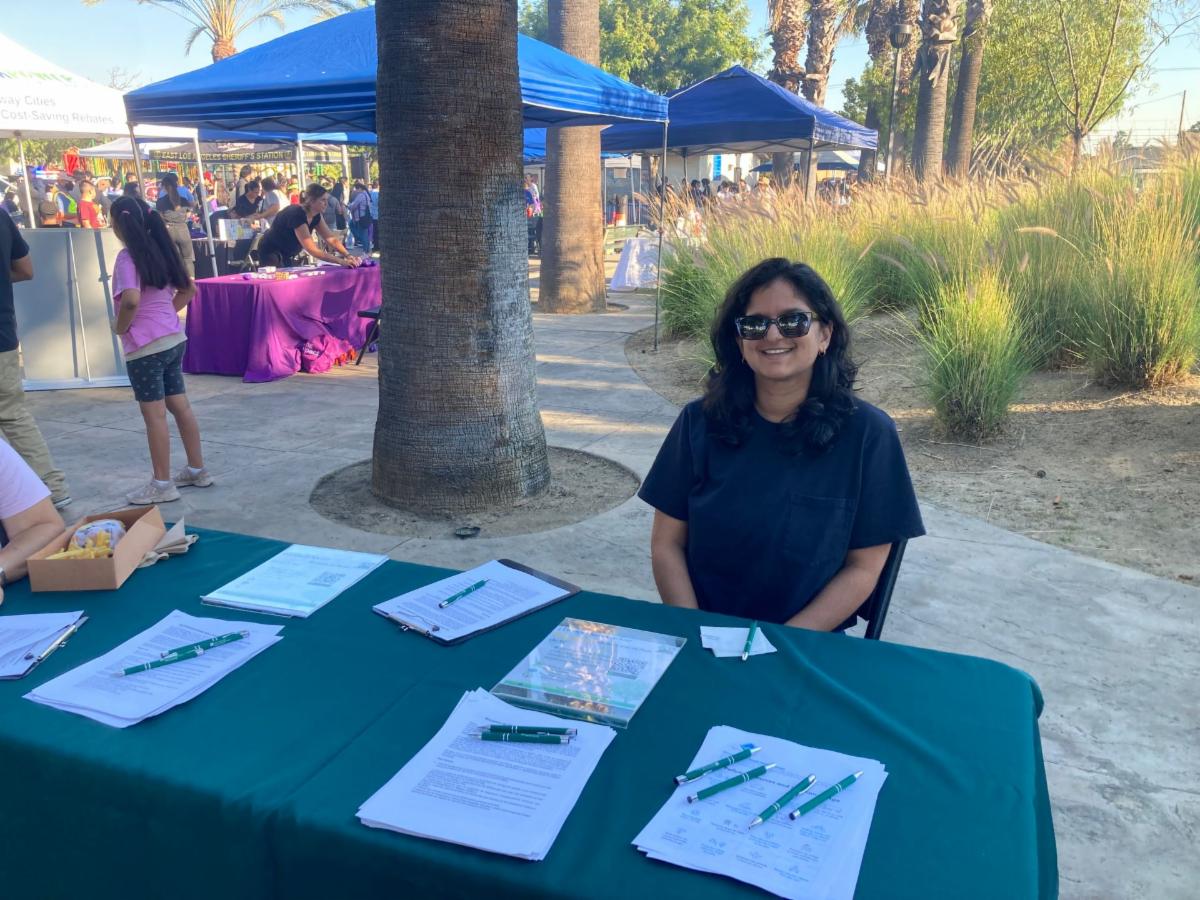 Person with sunglasses smiling while sitting at table with green tablecloth pens and papers on top of the table