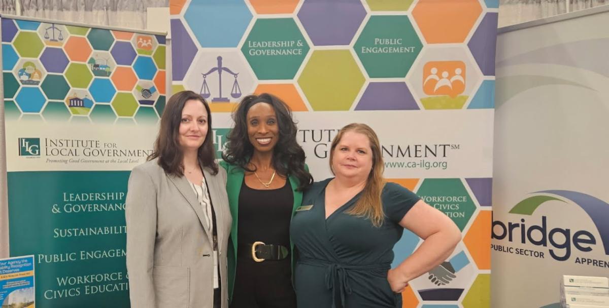 Hanna Stelmakhovyck Erica L Manuel and Melissa Kuehne smiling and standing in front of ILG expo booth