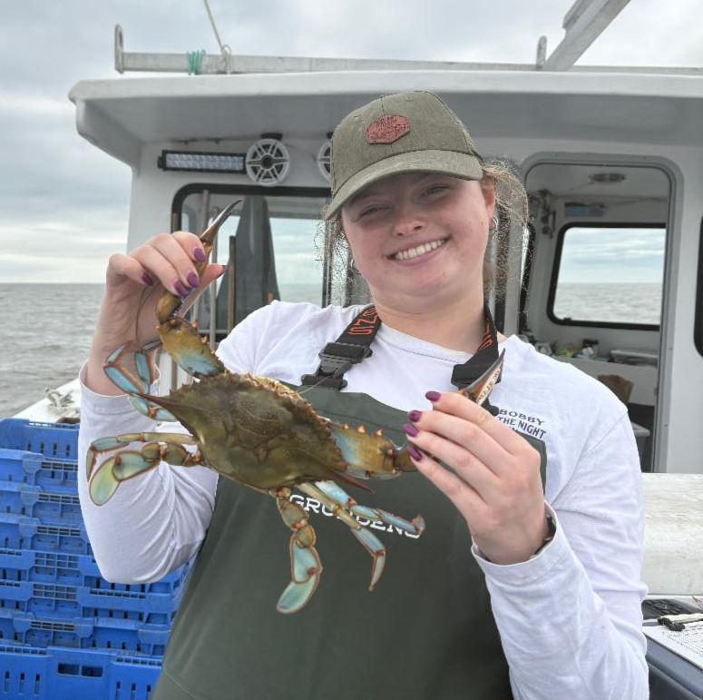 Female graduate student on a vessel holding a blue crab.