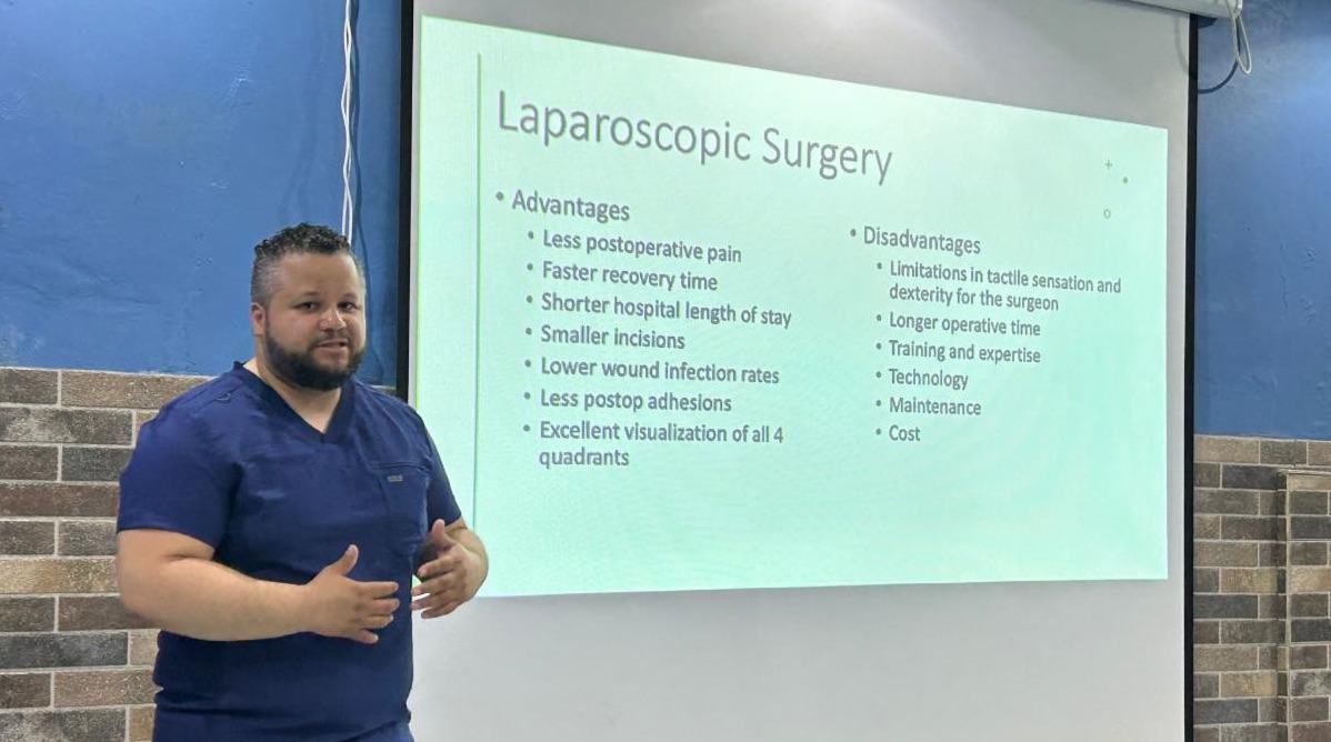 A man wearing medical scrubs stands by a large screen showing information about laparoscopic surgery.