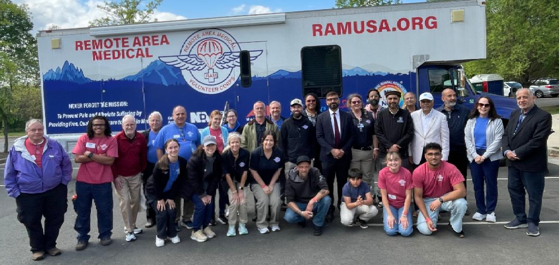About two dozen volunteers pose in front of a RAM USA trailer.