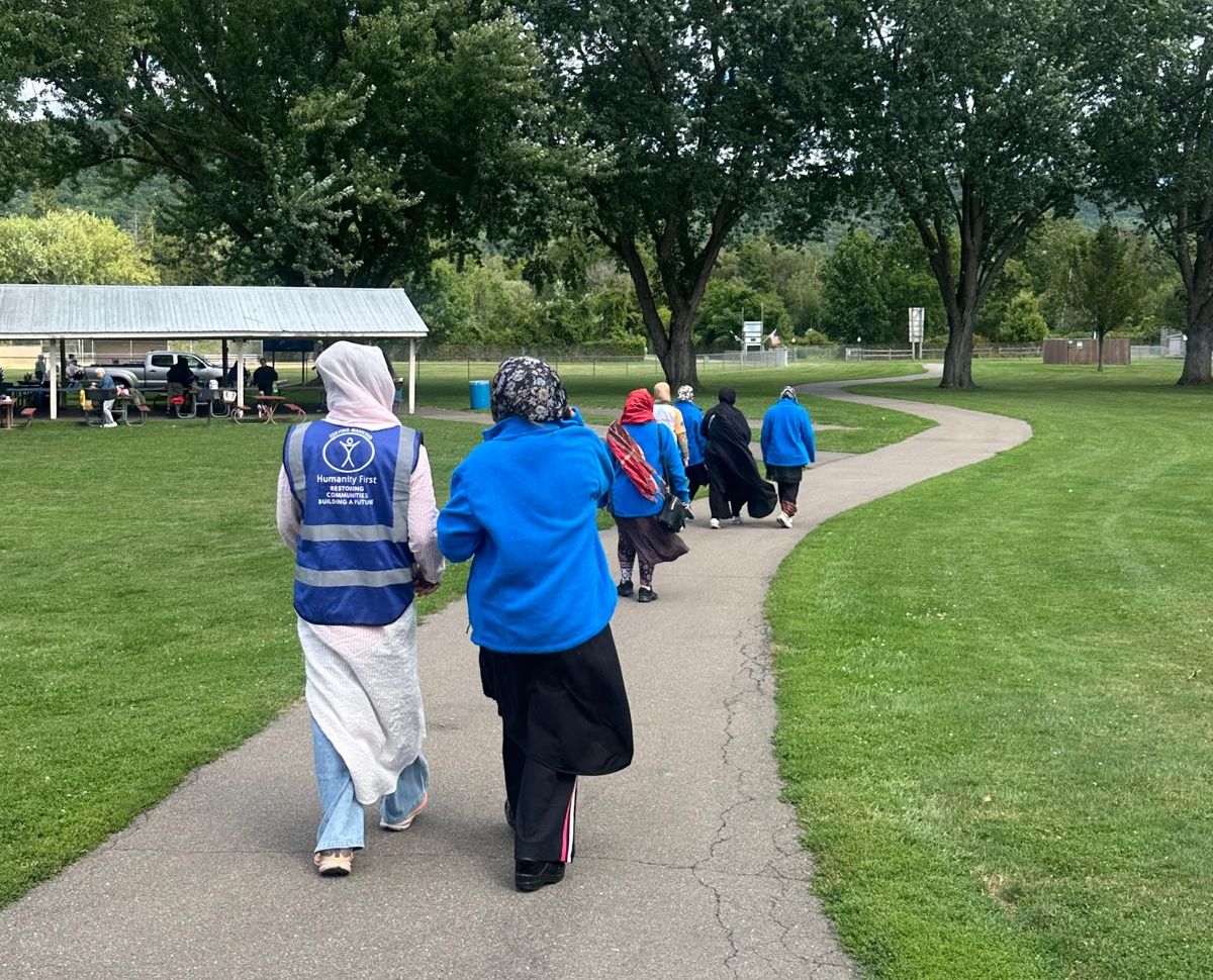 Ladies wearing long clothes and blue jackets or blue humanity first vests walking outside along a well developed path.
