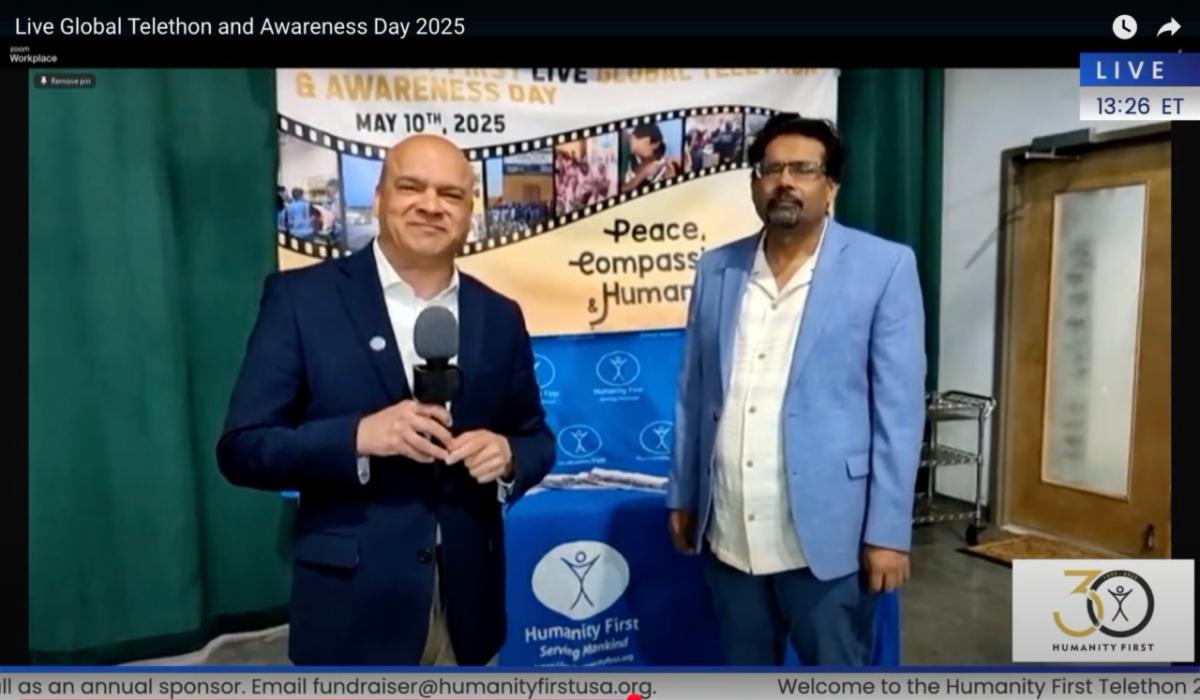 Two men in suits stand in front of a banner for the Humanity First Live Global Telethon