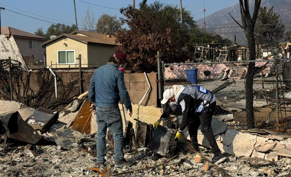 An HF volunteer works with a homeowner to move heavy debris from his burned home.