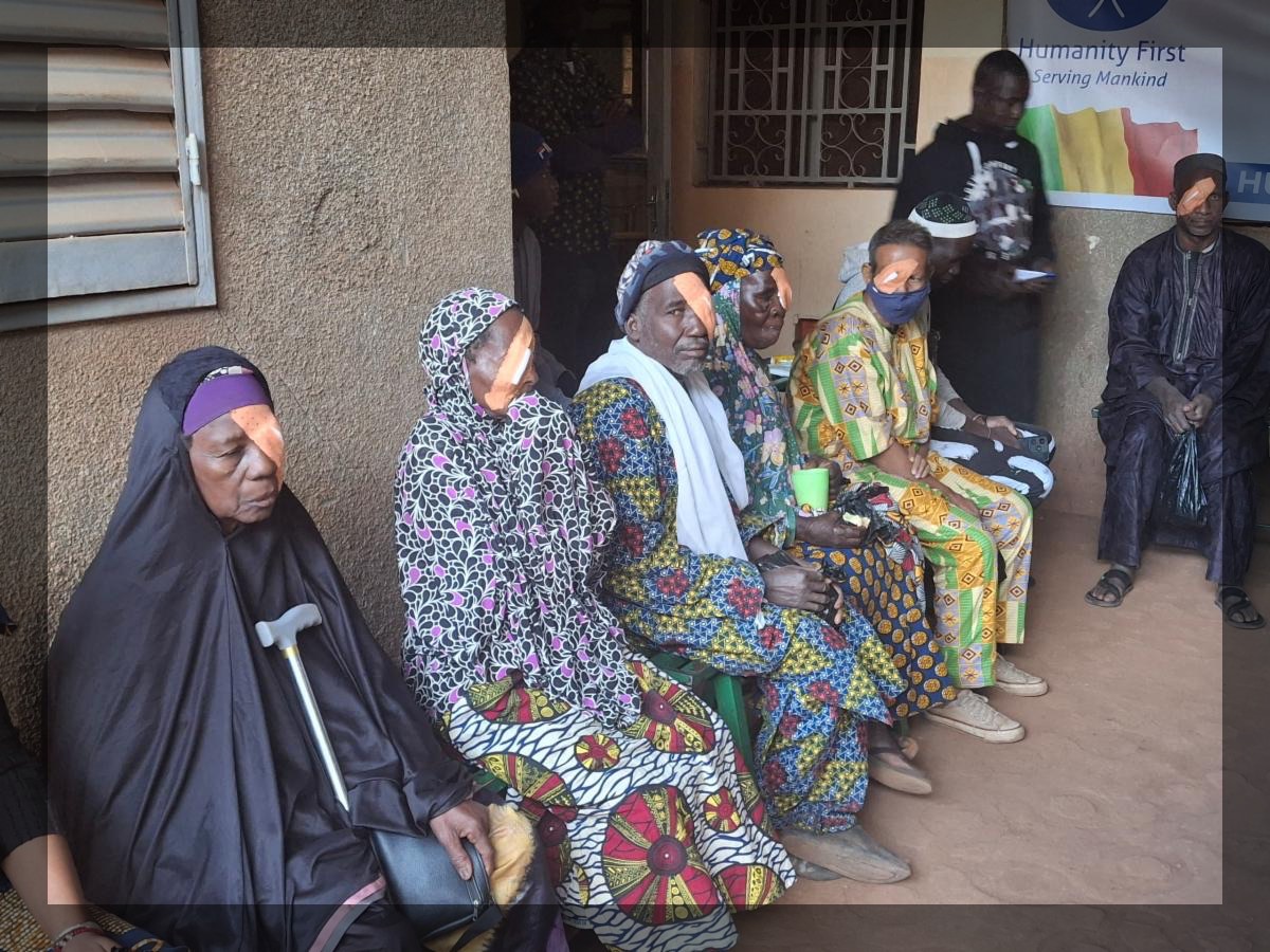 Elderly people in Mali sit in a row of chairs. Each has a bandage over one of their eyes as they recover after surgery.