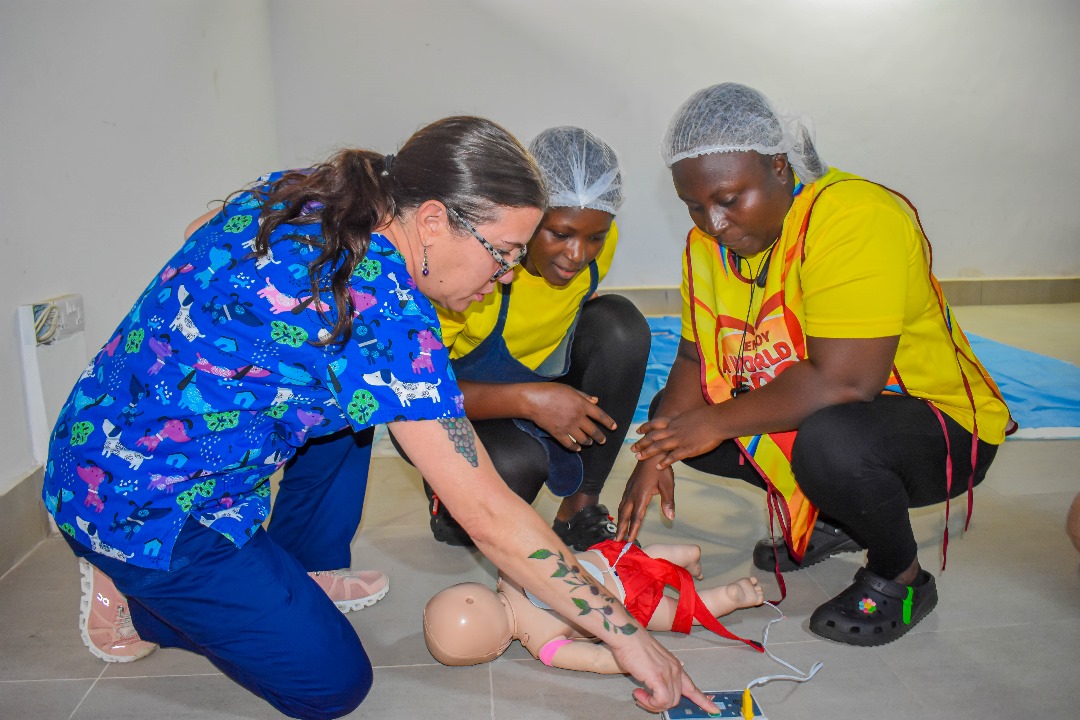 Three people look at a baby mannequin with an AED machine attached to it to practice this first aid.