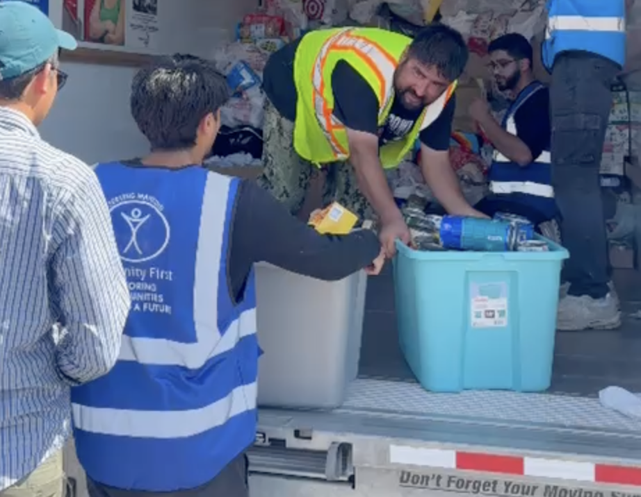 People wearing blue vests unload tubs of supplies from a truck.