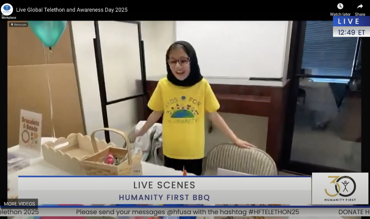 A young girl wearing a Kids for Humanity yellow tee shirt gestures to baskets of craft materials on a table ready for kids to create with.
