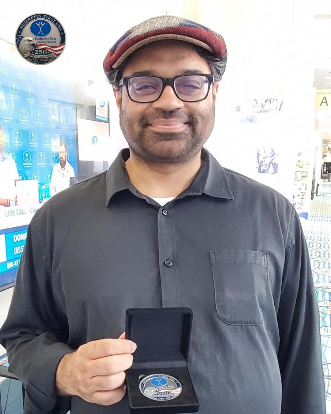 A man poses holding a Humanity First USA limited edition Challenge Coin in its display case.