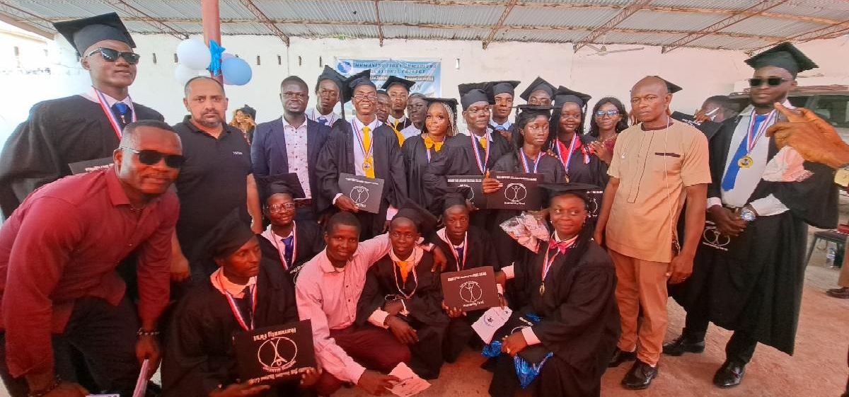One group of two dozen people in suits and graduation gowns and hats holding folders showing the Humanity First logo