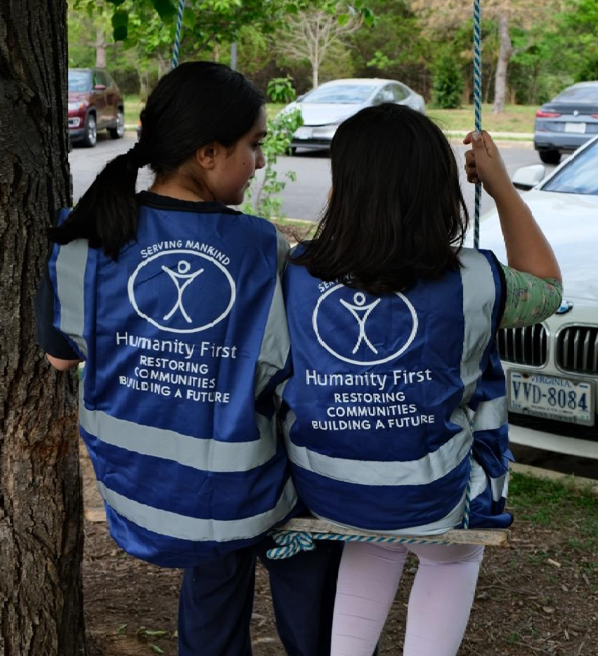 Two young girls wearing humanity first vests take a break from clinic volunteering on an outdoor swing.