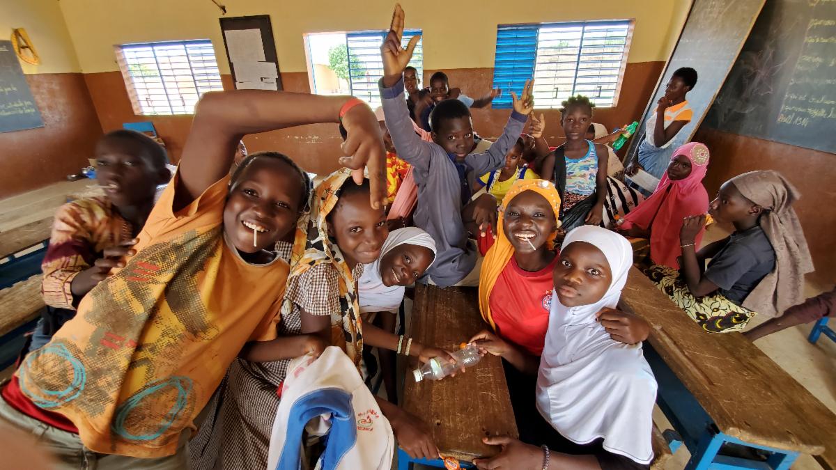 A group of elementary school children strike a fun pose for the camera from a set of long desks in a classroom.