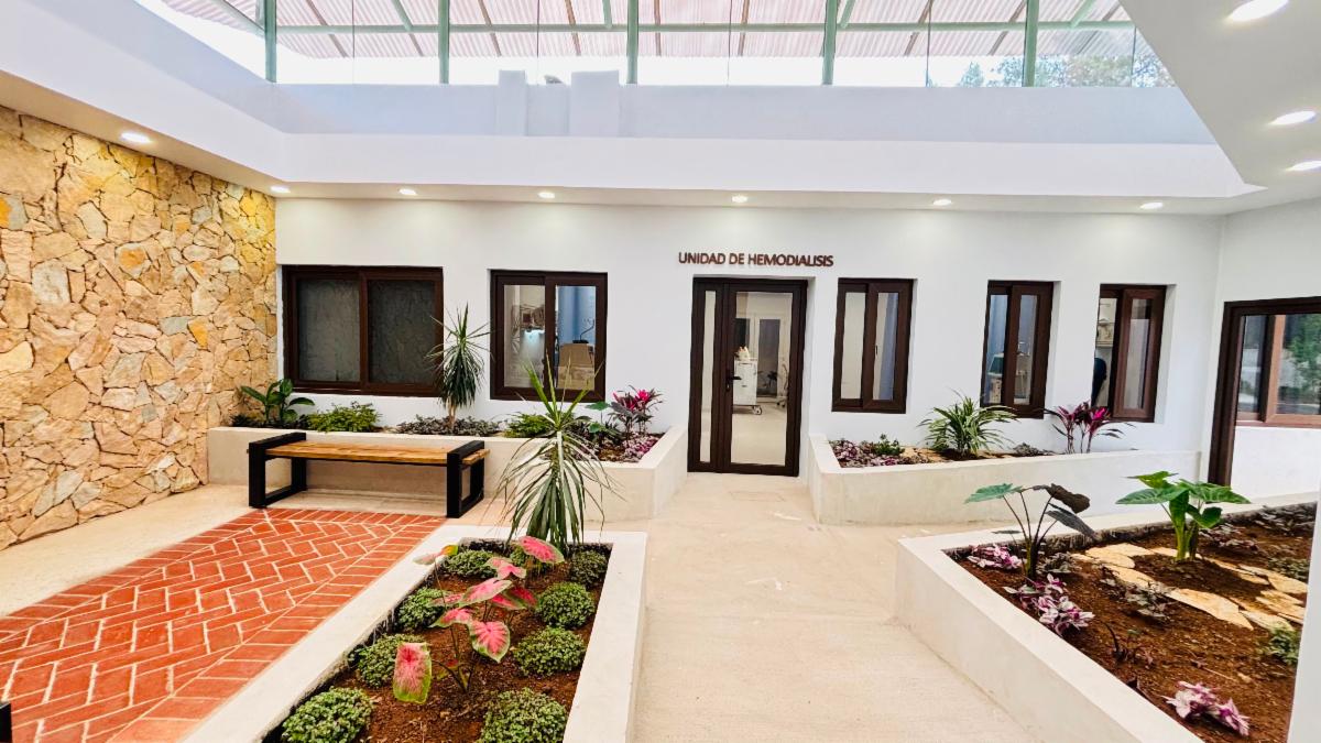 A brightly lit waiting area with a windows in the ceiling, indoor plant beds, and a stone wall lead to the entrance of the Unidad de Hemodialisis the Dialysis Centre at Nasir Hospital 